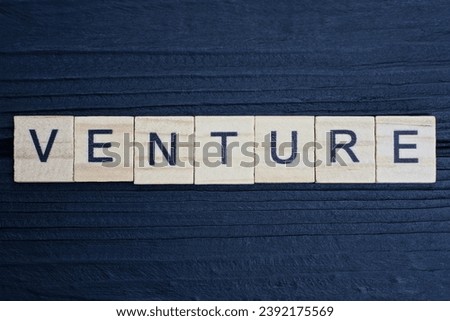 text the word venture from brown wooden small letters on a black table