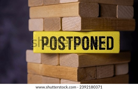 The word POSTPONED is written in a white notepad near a white cup of coffee on a light background. Royalty-Free Stock Photo #2392180371