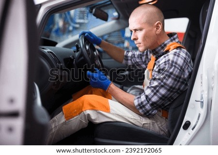 European male service engineer in uniform repairs a car steering wheel in a auto service Royalty-Free Stock Photo #2392192065