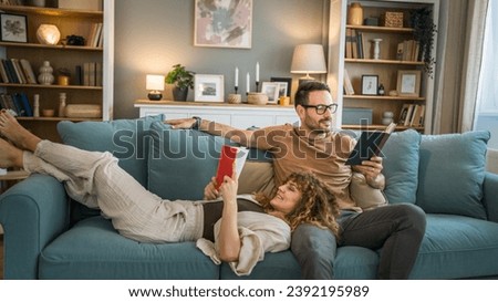 Adult couple man and woman Caucasian husband and wife in a relationship real book hold books on the sofa bed at home in the apartment reading leisure bonding family concept real people copy space Royalty-Free Stock Photo #2392195989