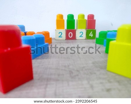 Colorful plastic toy blocks on wooden blocks with number 2024 on light wooden and white background, new year concept.
