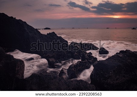 Beautiful beach view at sunset. rocks on the beach. Waves captured with a slow shutter speed. Long exposure with soft focus. Sky with clouds. Loh Ji Beach, West Java, Indonesia