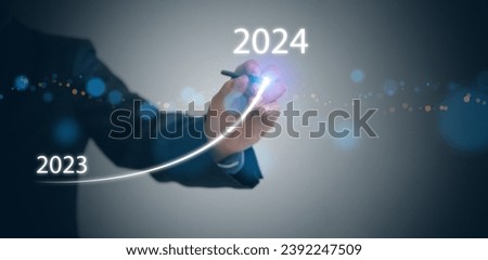 A businessman draws rising curve on virtual tech screen, from the end of 2023 rises to the start of 2024. Happy new year and welcome new business goals and  visions 