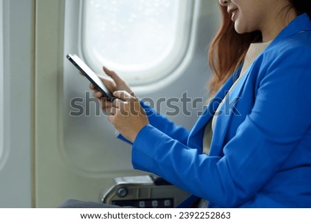 Happy Asian businesswoman uses mobile phone to check her meeting schedule during flight. Search information, take photo, check in, online chat. Technology concept, lifestyle.