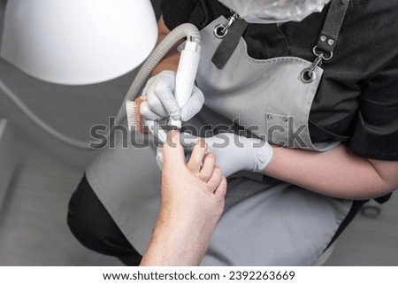 The process of filing off a thickened old nail from the fingers of an elderly woman. Procedure podologist.  Royalty-Free Stock Photo #2392263669
