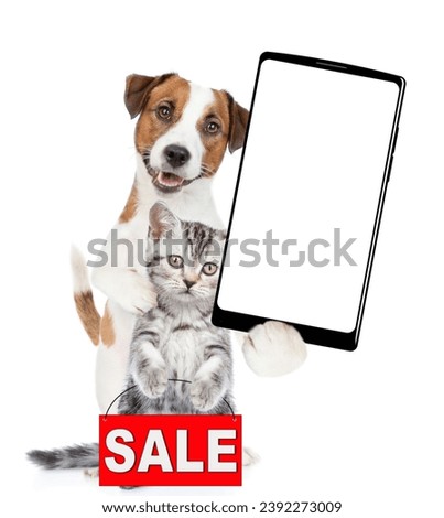 Smart Jack russell terrier puppy  hugs tabby kitten and shows big smartphone with white blank screen in it paw. Cat shows signboard with labeled "sale". isolated 