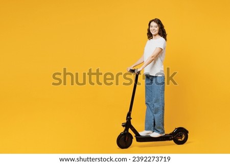 Side profile view young Caucasian woman she wear white blank t-shirt casual clothes driving electric scooter look camera isolated on plain yellow orange background studio portrait. Lifestyle concept