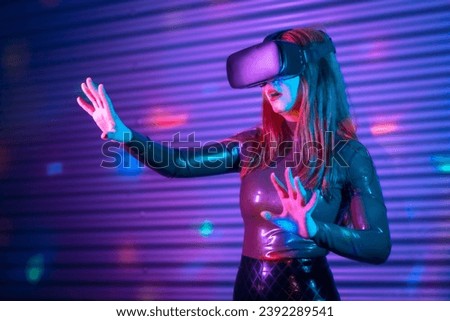 Blonde woman gesturing while wearing VR goggles in an urban night space with neon lights Royalty-Free Stock Photo #2392289541