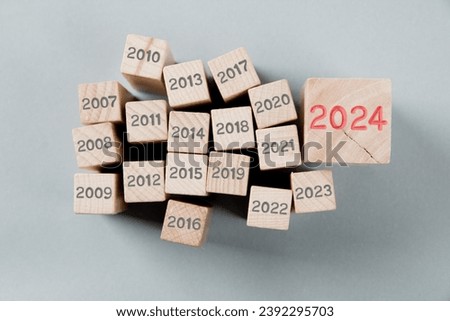 Photo of wooden block group with gray numbers of passed years and one of them standing out with red number 2024 imprinted on wooden surface. New Year concept.