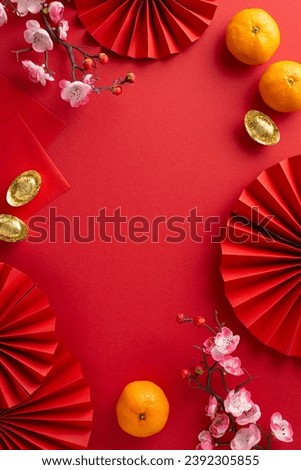 Tradition-rich Chinese New Year display. Vertical top view fans, feng shui decor, coins, sycee, Hong Bao envelopes, tangerines, and sakura arranged on a red surface with frame for text
