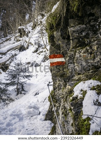 Via ferrata rock climbing route during winter snow with red white tourist sing symbol painting on a rock, Carinthia, Austria