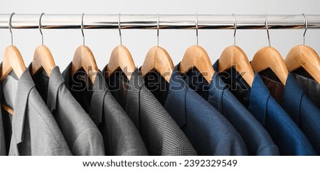 Hanger with different stylish male suits on light background