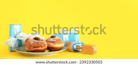 Tasty donuts, dreidels and gifts on yellow background with space for text. Hanukkah celebration