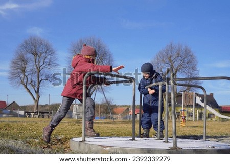 European snowless winter. Children playing on playground, balance on a merry-go-round, Background of bare trees under a bright blue sky. Balance and Coordination learn, Social Development concept