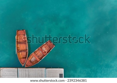 An artistic, perpendicular view of two wooden boats at a pier on the blue-green surface of Lago di Braies in the Dolomites. Ideal for poster projects.