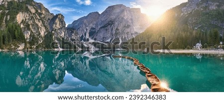 Panoramic photo of Lago di Braies, Pragser Wildsee in the Dolomites. View of the whole green-blue lake through wooden boats on the mountain peak and the setting sun.  Royalty-Free Stock Photo #2392346383
