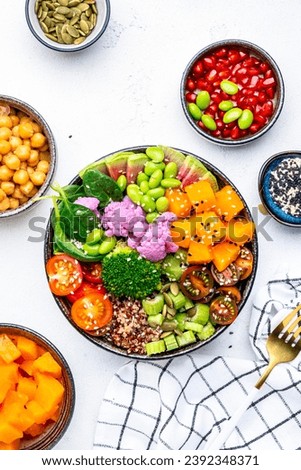 Vegan buddha bowl with baked pumpkin, quinoa, tomatoes, spinach, celery, radish, soybeans, edamame, tofu, cauliflower, broccoli and sesame seeds, white table background, top view. Autumn or winter hea