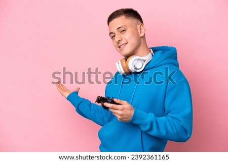Young brazilian man playing with a video game controller isolated on pink background extending hands to the side for inviting to come