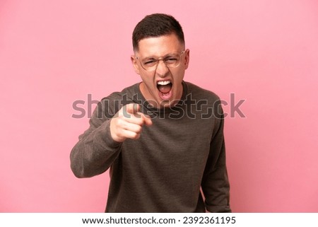 Young Brazilian man isolated on pink background frustrated and pointing to the front