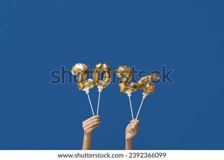 Female hands with figure 2024 made of balloons on blue background