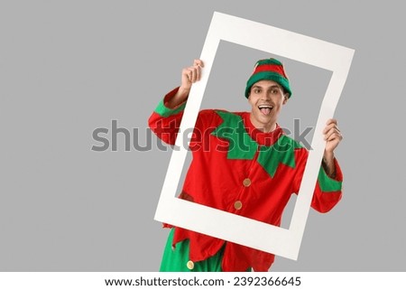 Handsome young man in elf's costume with frame on grey background