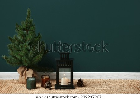Lantern with burning candles and Christmas tree on floor near color wall