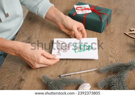 Mature woman with greeting card for Christmas celebration at table, closeup