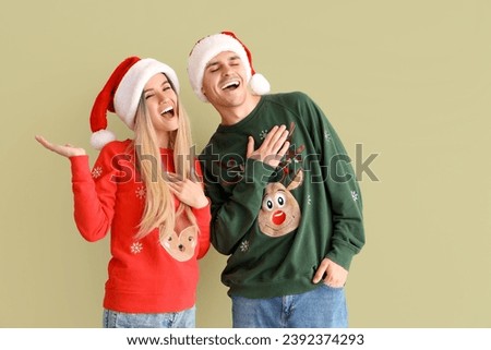 Young couple in Santa hats and Christmas sweaters on green background
