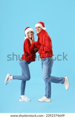 Happy young couple in Santa hats holding hands on blue background
