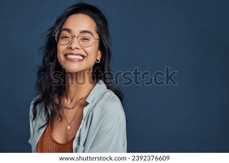 Casual young multiethnic woman with eyeglasses smiling at camera on blue background. Close up face of happy mixed race girl laughing with eyeglasses isolated with copy space. Beautiful girl laughing. Royalty-Free Stock Photo #2392376609