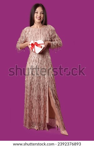 Beautiful young Asian woman with gift box for Valentine's Day on purple background