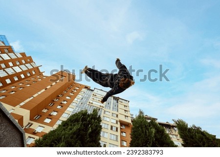 Athlete man, young guy jumping high, making back-flip over city, high-rise buildings and sky view in public park. Eye fish filter. Concept of lifestyle, extreme kinds of sport, freestyle, activity. Ad