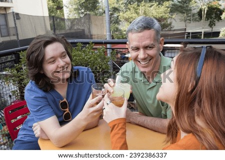 Grey haired dad with children are cheering and holding drinking glasses. Fathers Day. Concept of family, relationship, connection, enjoyment. Royalty-Free Stock Photo #2392386337