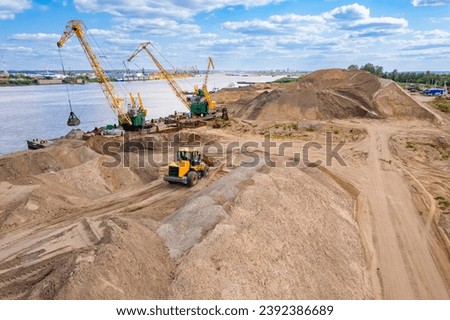Aerial top view yellow excavator working on sand quarry, industrial crane unloads barge. Concept Open pit mine industry. Royalty-Free Stock Photo #2392386689