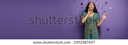 surprised young indian woman under confetti rain on purple backdrop with hand near face, banner