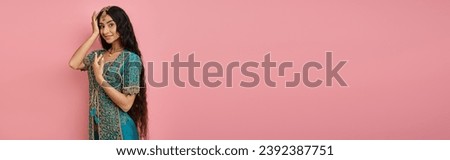 attractive indian woman in national costume posing with hand near face and smiling at camera, banner
