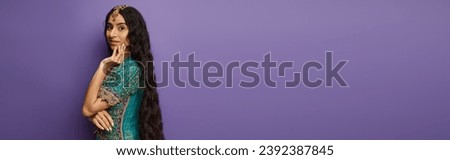 beautiful jolly indian woman in blue traditional sari looking at camera on purple backdrop, banner