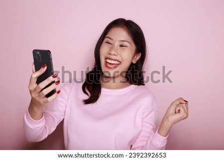 Posing alone on a light pink background. Asian woman is excited about something on the phone The young woman felt extremely happy. half body photo of nice positive lady.