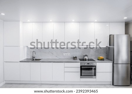 Front view of a modern white kitchen with many cabinets and all the necessary built-in appliances