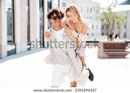 Young smiling beautiful woman and her handsome boyfriend in casual summer clothes. Happy cheerful family. Couple posing in street at sunny day. Female sits at his back. piggyback riding