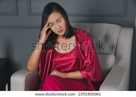 The woman in the red nightwear is sitting with a headache in the bedroom of the resort. Royalty-Free Stock Photo #2392405081