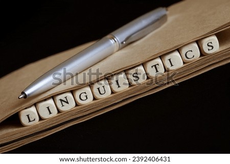 Word linguistics, made up of wooden cubes, and an eco-friendly notebook on dark. Concept of scientific research in linguistics and teaching linguistics at school or college. Photo. Close-up
