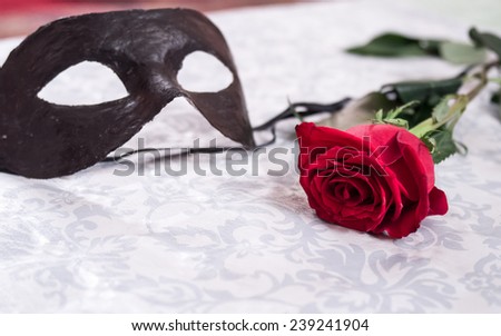 Black venetian masquerade mask at the red rose on white textured background