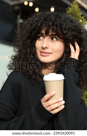 Happy young woman in stylish black sweater with cup of coffee outdoors