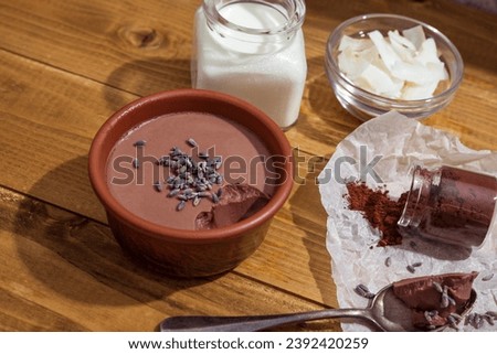 Chocolate panna cota with coconut milk, vegan chocolate pudding with agar and extra-dark cocoa powder. Coconut milk, cocoa powder, coconut chips and dry lavender next to a delicious Italian dessert Royalty-Free Stock Photo #2392420259