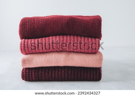 Sweaters. Red, pink sweaters stacked on gray background. Royalty-Free Stock Photo #2392434327