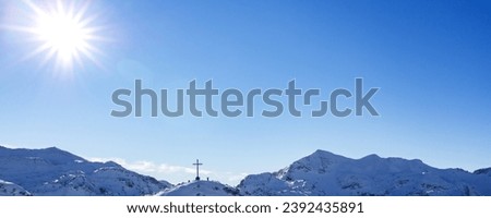 Banner cross on a snow-covered mountain on the background of a blue sky with the sun
