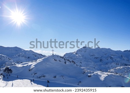 The sun in the blue sky, a winter day, a cross on a low mountain above the ski slope