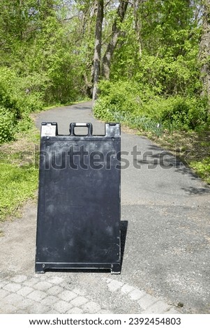Blank black sign on a curved asphalt path through a wooded area