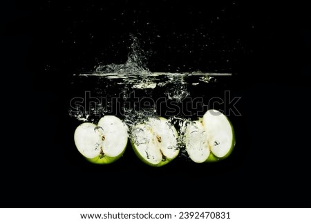 Three sliced green apples falling into water with a black background creating bubbles and a splash